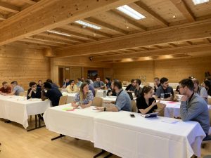 Members of the CuPiD network hold one-to-one discussions during the conference in Alpbach. They are sat at tables covered in white tablecloths, and the room's walls and ceiling are all wood.
